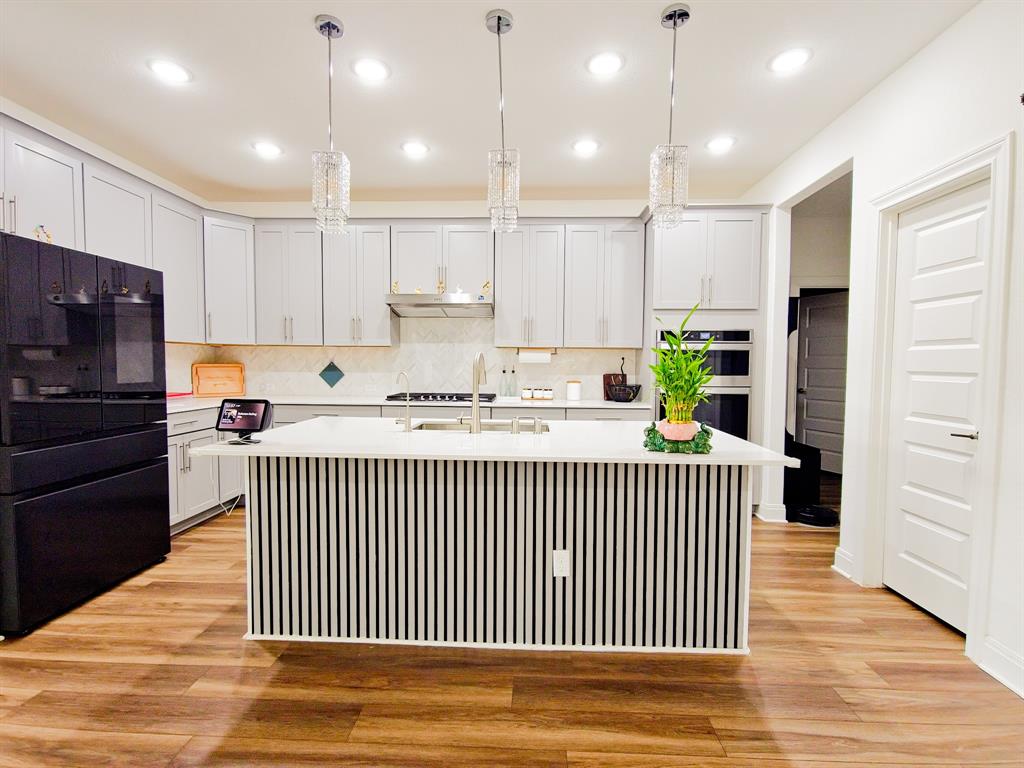 332 Turnbuckle Bend Leander, TX 78641 - Photo 15 of 34 Modern kitchen featuring a central island with vertical paneling, light gray cabinetry, stainless steel appliances, and wood-finish flooring