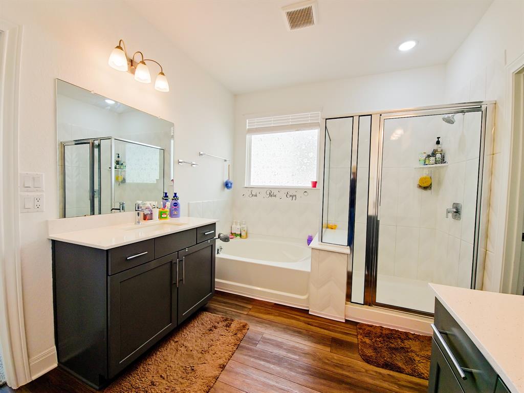 332 Turnbuckle Bend Leander, TX 78641 - Photo 21 of 34 Bathroom featuring a dark wood-finish vanity with a light countertop, a built-in bathtub, a glass-enclosed shower, and wood-finish flooring