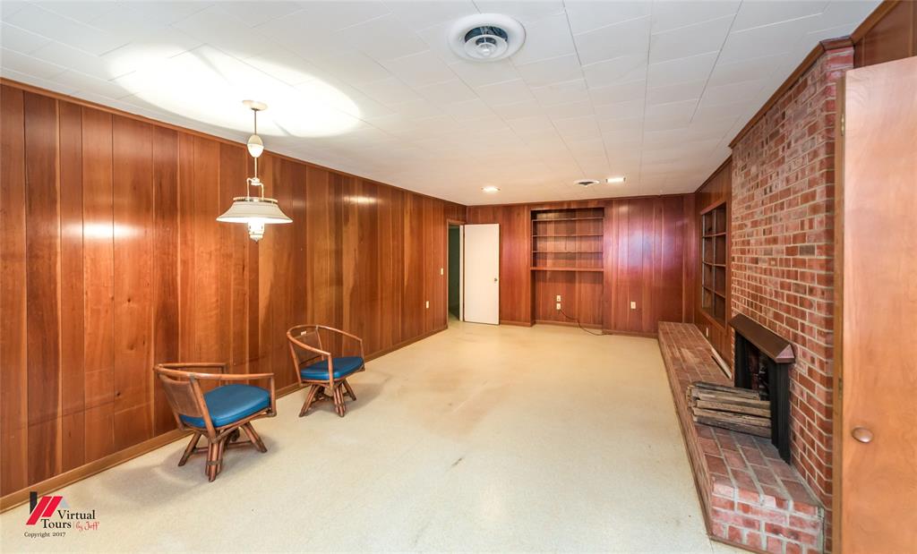 205 7th Street Northeast Springhill, LA 71075 - Photo 19 of 40 Wood-paneled walls featuring a built-in bookshelf, a brick fireplace with a raised hearth, and a ceiling-mounted light fixture