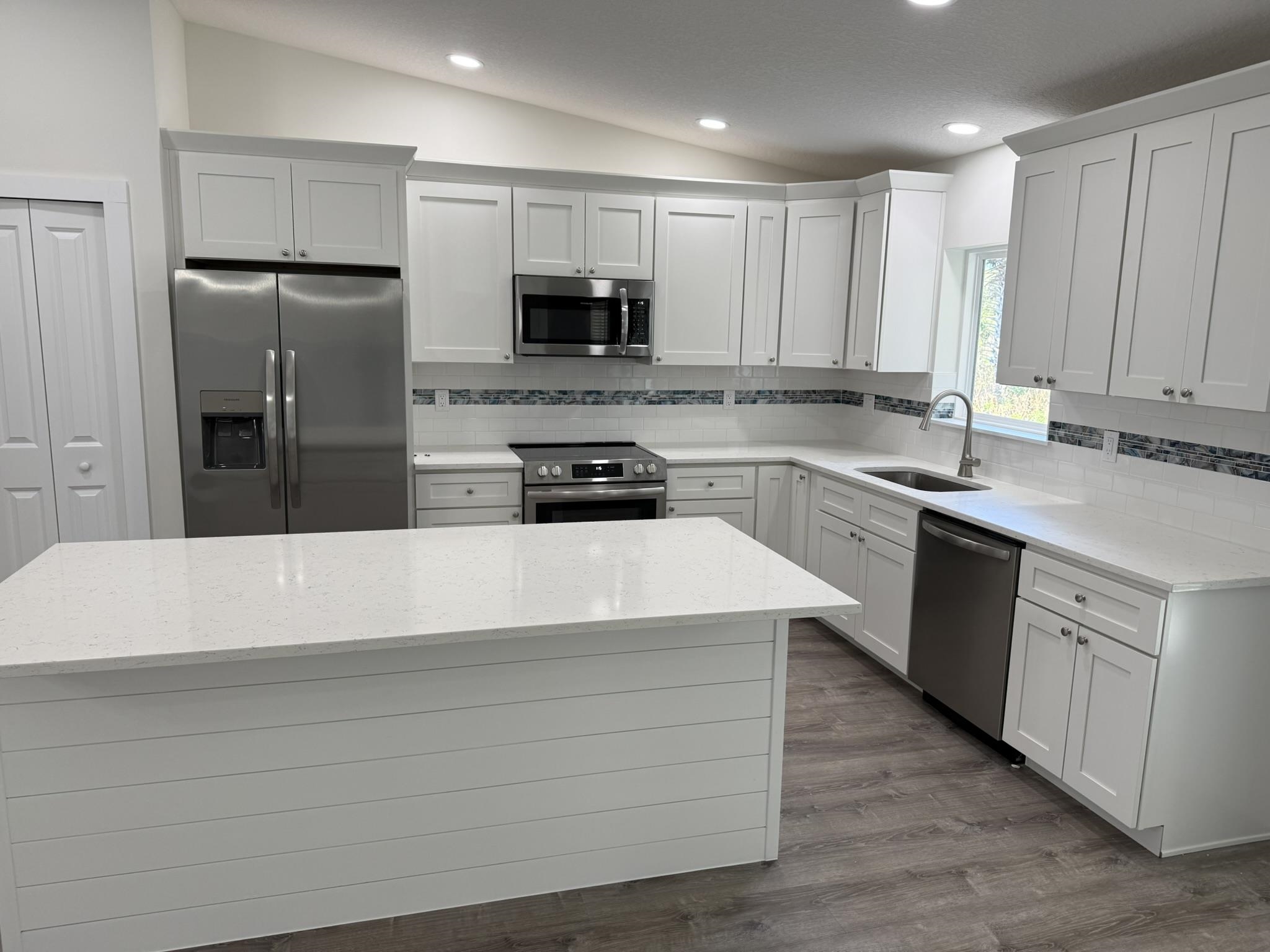 611 Queen Road St. Augustine, FL 32086 - Photo 2 of 17 Kitchen featuring stainless steel appliances, backsplash, lofted ceiling, white cabinets, and quartz countertops