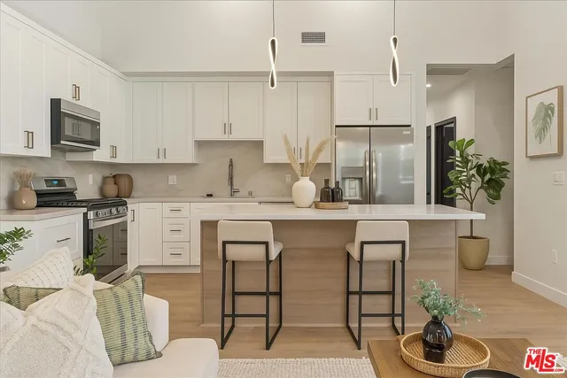 a kitchen with stainless steel appliances kitchen island granite countertop a refrigerator a stove a sink and white cabinets with wooden floor