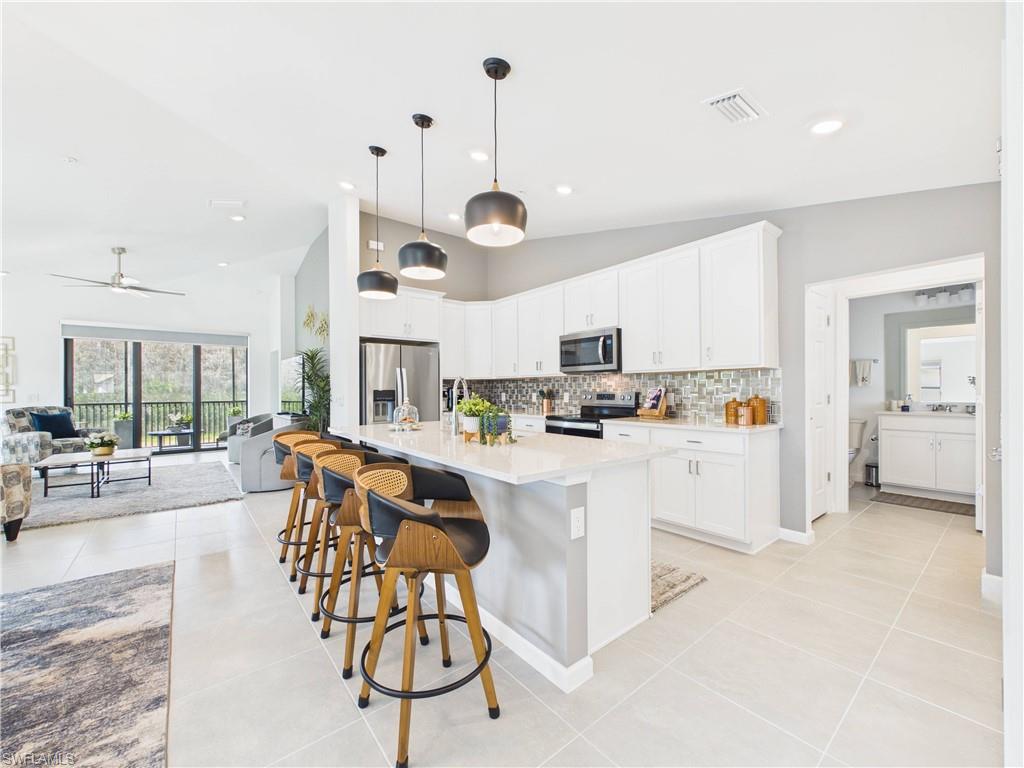 5683 Mayflower Way, Unit 908 Ave Maria, FL 34142 - Photo 1 of 37 Kitchen with stainless steel appliances, a center island with sink, a breakfast bar, white cabinets, and vaulted ceiling