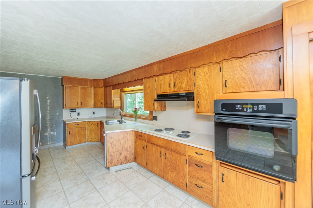 Kitchen featuring oven, sink, stainless steel fridge, white electric stovetop, and light tile patterned flooring