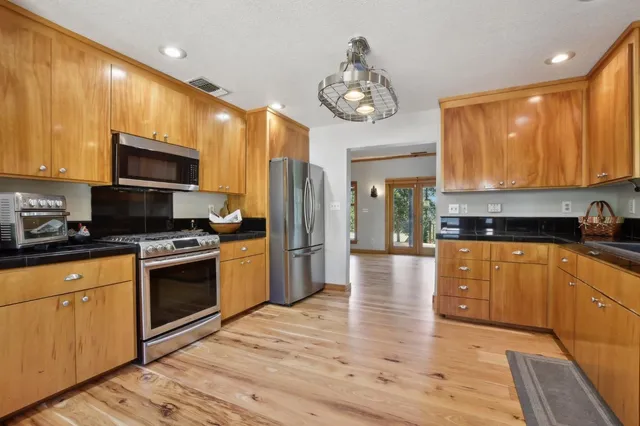 a large kitchen with stainless steel appliances granite countertop a stove top oven a refrigerator a sink and dishwasher with wooden floor