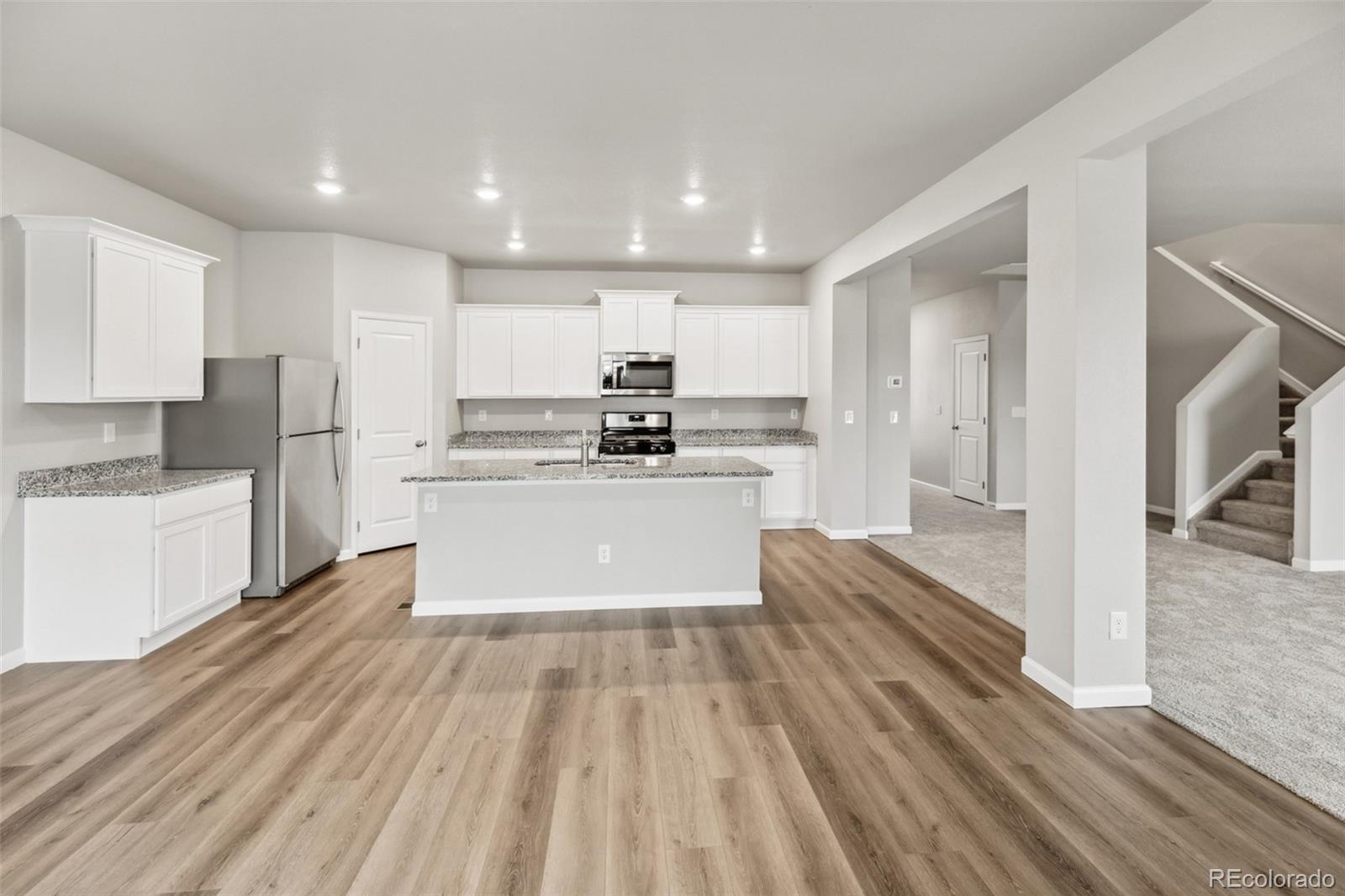 2220 Christina Street Fort Lupton, CO 80621 - Photo 6 of 42 a large kitchen with kitchen island a stove a refrigerator a sink dishwasher a oven with white cabinets and wooden floor