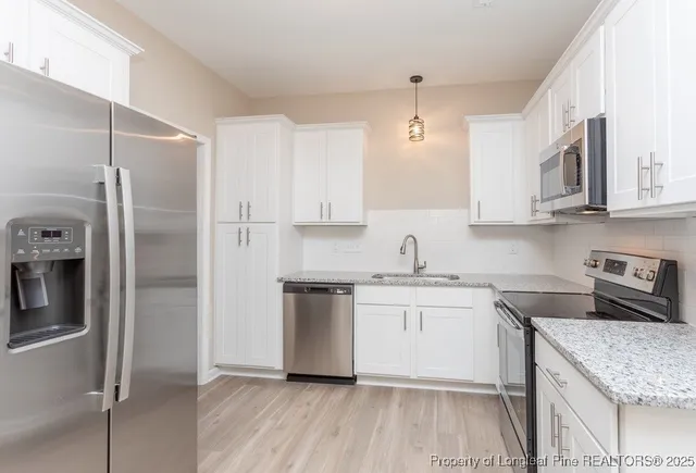 a kitchen with stainless steel appliances granite countertop a refrigerator a sink a stove and white cabinets with wooden floor