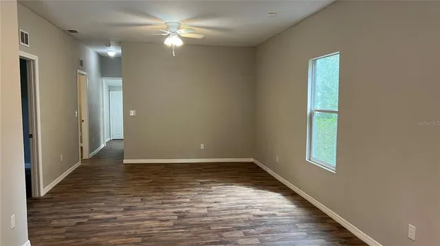 a view of an empty room with window and chandelier fan