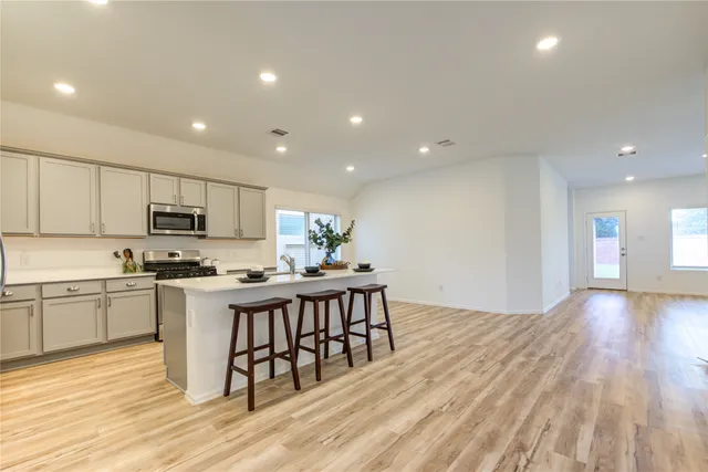 a kitchen with stainless steel appliances granite countertop a stove top oven a sink dishwasher and a dining table with wooden floor