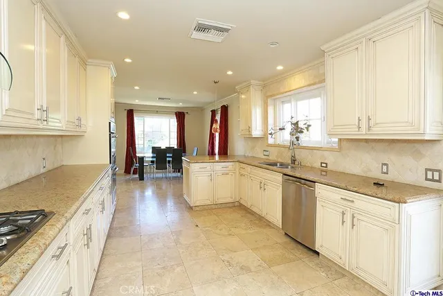 a large kitchen with stainless steel appliances granite countertop a large counter top a stove a sink a refrigerator and white cabinets with wooden floor