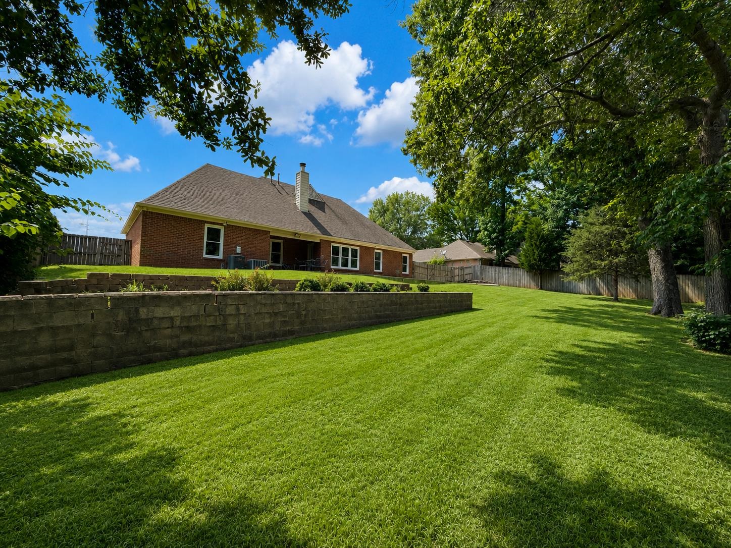 326 South Sanga Road Cordova, TN 38018 - Photo 31 of 32 Expansive backyard featuring a lush green lawn, mature trees providing natural shade, and a brick retaining wall with landscaping