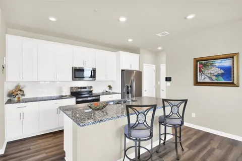a kitchen with stainless steel appliances granite countertop a stove a sink a refrigerator with white cabinets a dining table and chairs