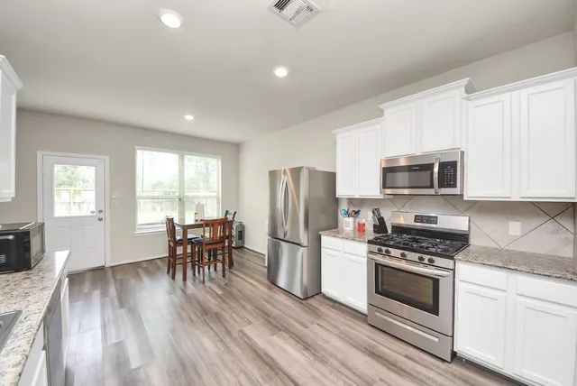 a kitchen with stainless steel appliances a stove a sink a refrigerator cabinets and dining table