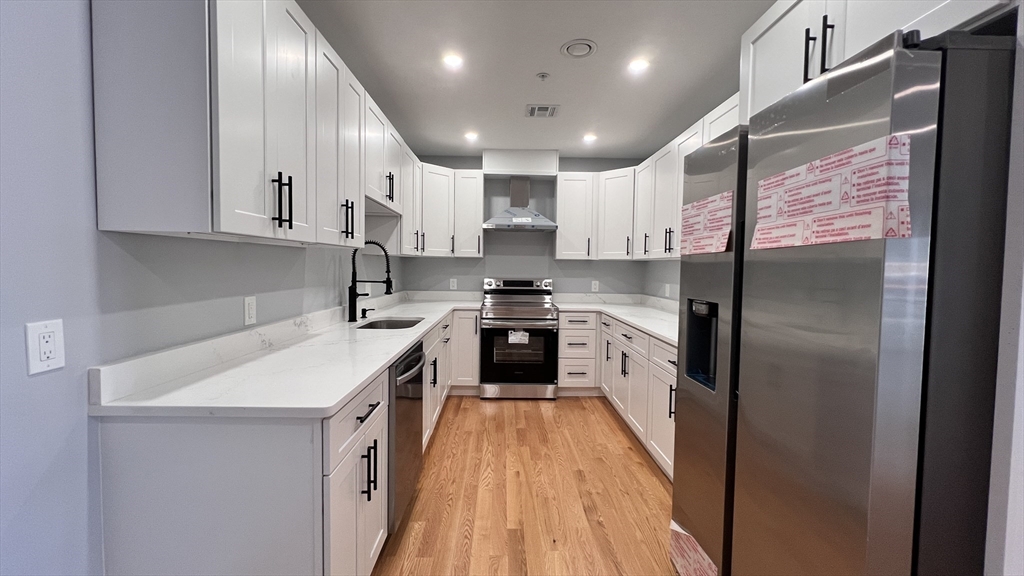 585 Washington Street, Unit MODEL2 Quincy, MA 02169 - Photo 2 of 10 a kitchen with stainless steel appliances granite countertop a refrigerator a sink dishwasher a stove and white countertops with wooden floor