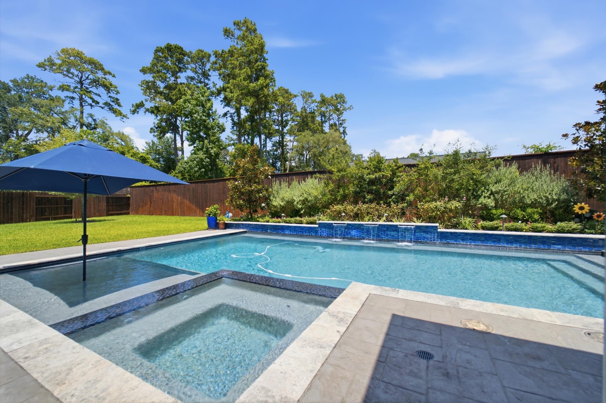 23722 Thortons Park Lane Spring, TX 77389 - Photo 41 of 48 This backyard features a spacious swimming pool with a connected hot tub, surrounded by a neatly landscaped garden and privacy fence. A large umbrella provides shade, offering a perfect spot for relaxation and outdoor enjoyment.