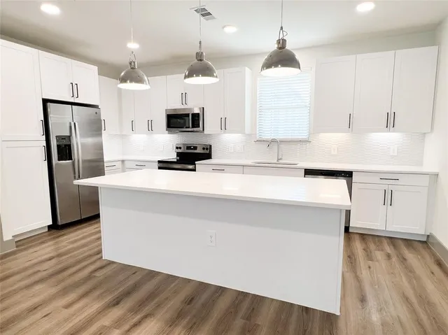 a kitchen with stainless steel appliances a refrigerator a sink a stove a microwave and wooden floor