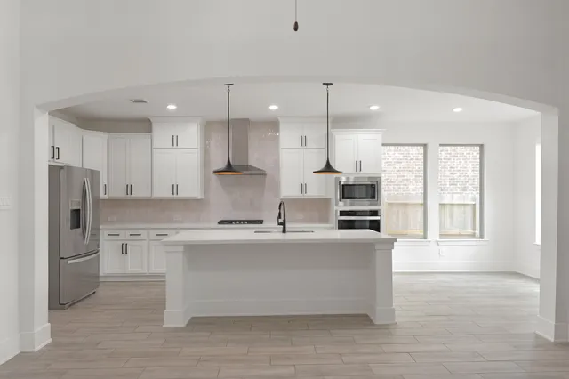 a large kitchen with stainless steel appliances granite countertop a stove a sink a refrigerator and white cabinets with wooden floor