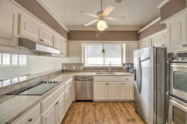 a kitchen with a sink dishwasher a refrigerator with white cabinets and wooden floor