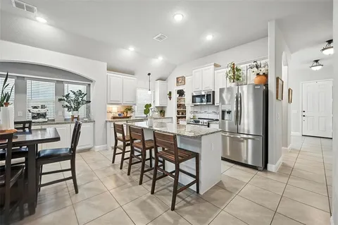 a kitchen with stainless steel appliances a refrigerator a stove top oven and a dining table with wooden floor