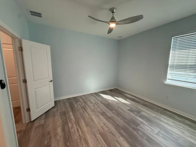 an empty room with wooden floor fan and windows