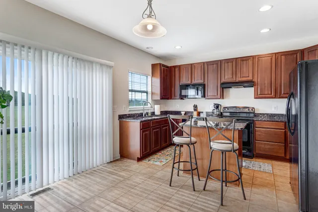 a kitchen with stainless steel appliances granite countertop white cabinets a sink a stove a dining table and chairs