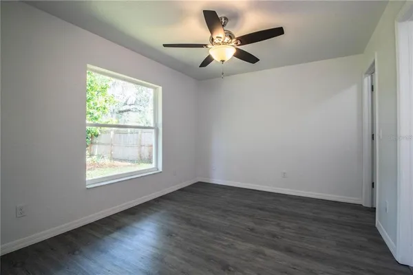 an empty room with wooden floor chandelier fan and windows