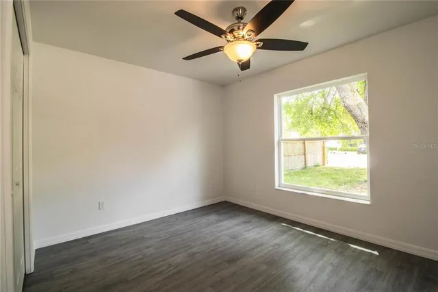 an empty room with wooden floor fan and windows