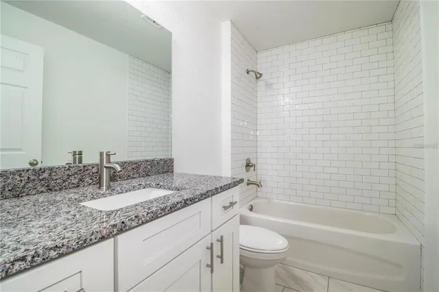 a bathroom with a granite countertop sink a toilet and bathtub