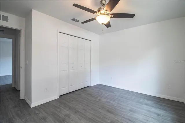 an empty room with wooden floor fan and windows