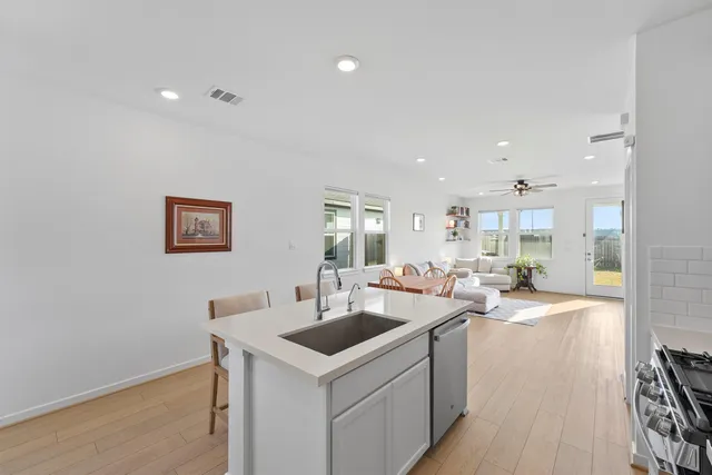 a living room with stainless steel appliances kitchen island granite countertop a table chairs and a refrigerator