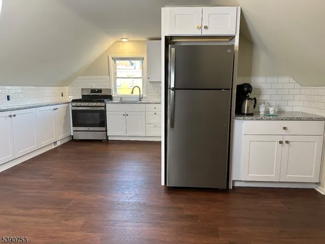 a kitchen with granite countertop a refrigerator stove and white cabinets