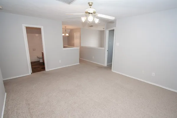an empty room with chandelier fan and kitchen view