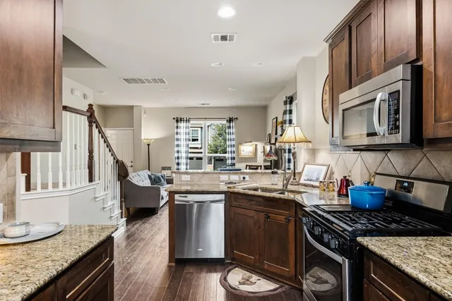 a kitchen with stainless steel appliances granite countertop a stove top oven a sink dishwasher and cabinets with wooden floor