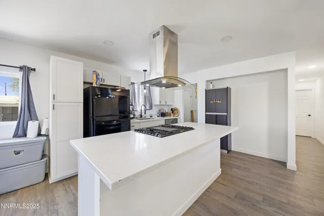 a large white kitchen with a refrigerator a stove a sink and a dining table with wooden floor