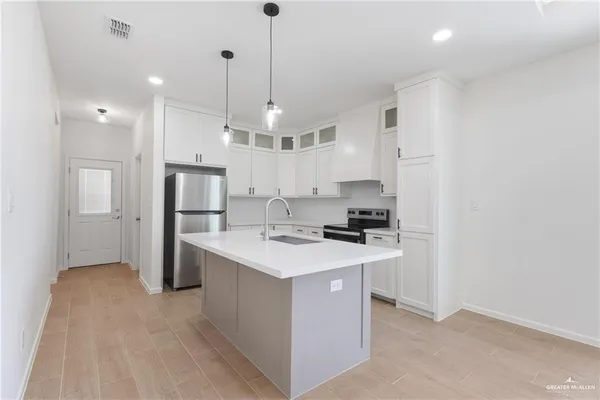 a kitchen with stainless steel appliances a refrigerator a sink dishwasher a stove and white cabinets with wooden floor