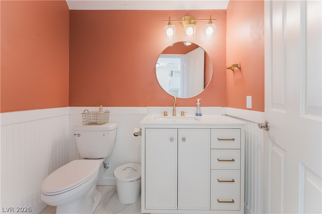8872 Chapman Point Las Vegas, NV 89129 - Photo 11 of 29 A vibrant bathroom features white wainscoting and a modern vanity, illuminated by stylish lighting.