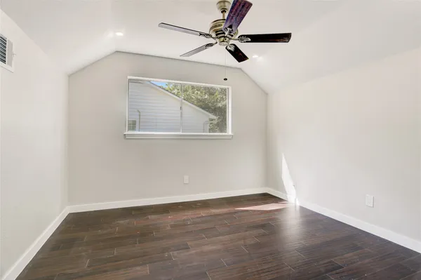 an empty room with wooden floor ceiling fan and windows