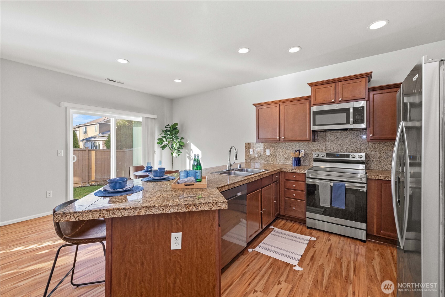 26219 243rd Place Southeast Maple Valley, WA 98038 - Photo 8 of 40 a kitchen with granite countertop a stove top oven a sink dishwasher and wooden cabinets with wooden floor