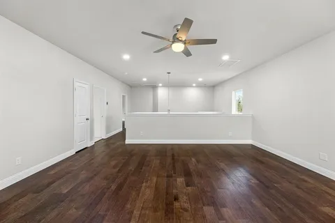 a view of an empty room with wooden floor and a ceiling fan