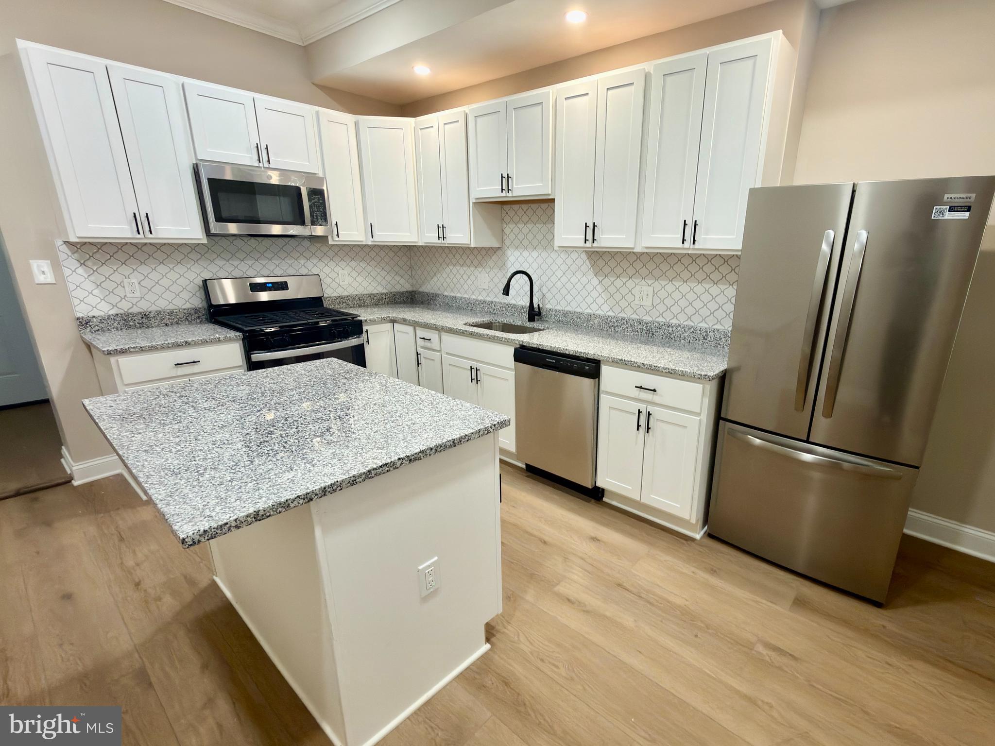 2129 Federal Street Baltimore, MD 21213 - Photo 4 of 27 a kitchen with granite countertop a refrigerator a stove a sink and white cabinets