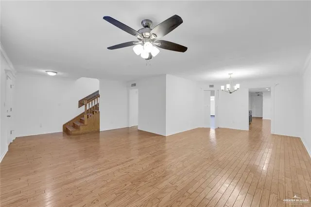 a view of an empty room with wooden floor and a ceiling fan