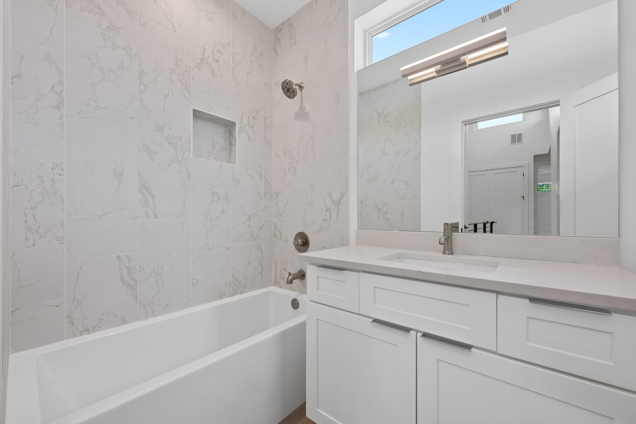 3614 Abbate Circle, Unit A Austin, TX 78721 - Photo 19 of 29 The bathroom features a built-in tub with a shower, a tiled shower surround with an integrated niche, a vanity with white cabinetry and a light-colored countertop, and a large mirror with overhead lighting