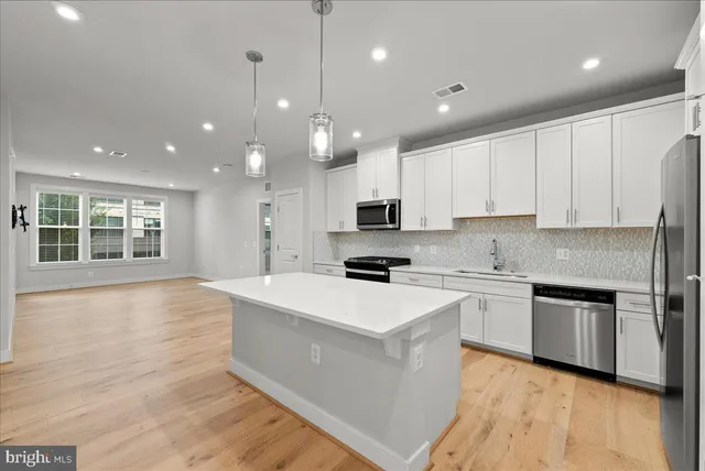 a large kitchen with stainless steel appliances granite countertop a stove top oven a sink dishwasher and white cabinets with wooden floor