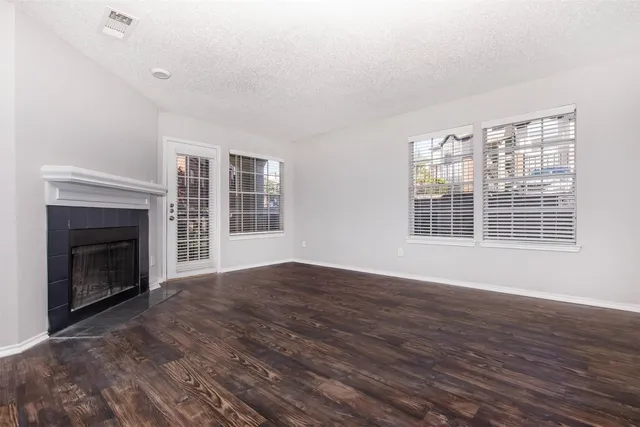 a view of an empty room with wooden floor fireplace and a window