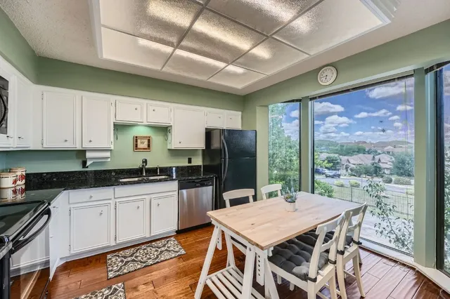 a kitchen with stainless steel appliances granite countertop a stove a refrigerator a sink a dining table and chairs with wooden floor