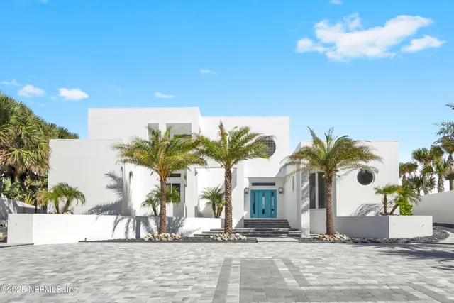 a view of a white house with a large tree and plants
