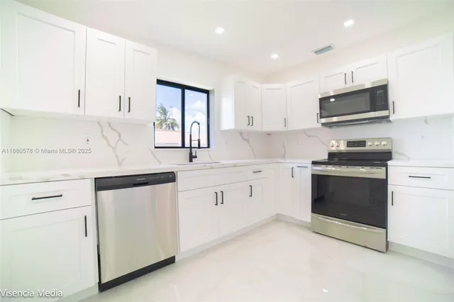 a large white kitchen with a refrigerator a stove a sink a window and white cabinets