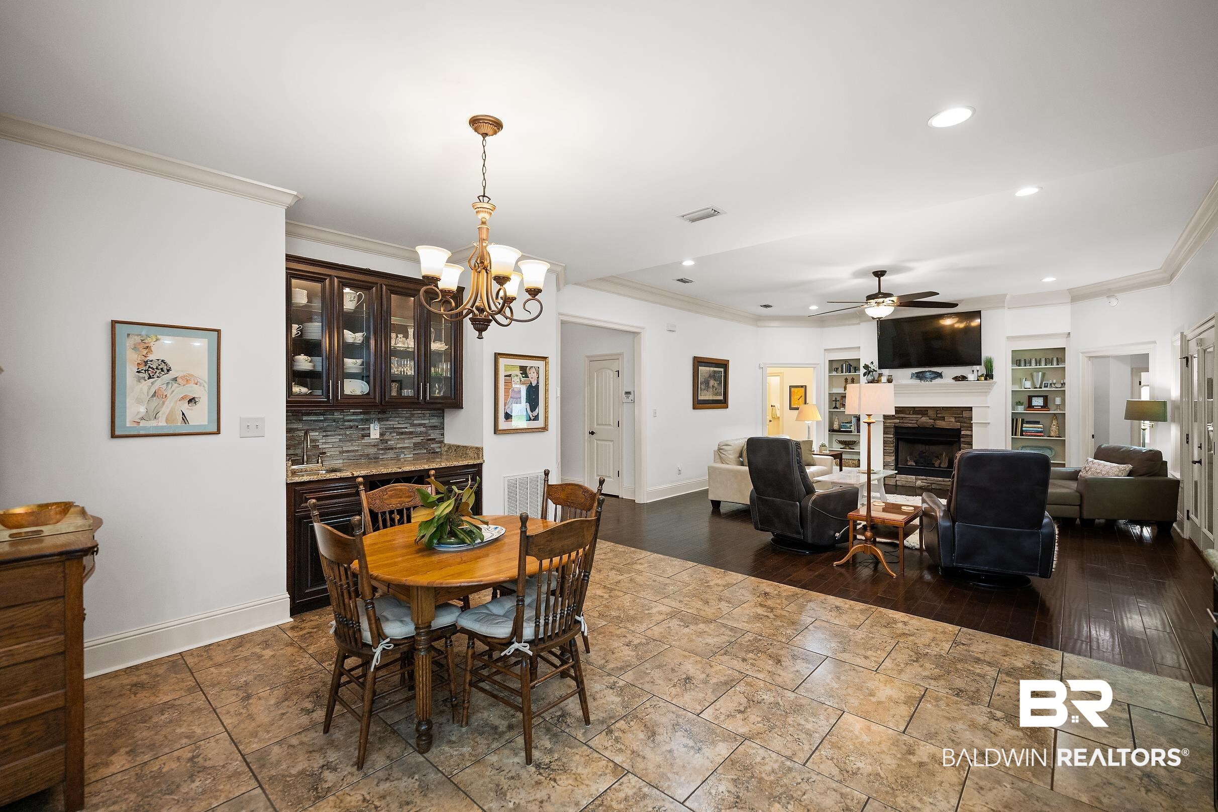 313 Pecan Ridge Boulevard Fairhope, AL 36532 - Photo 47 of 51 Open-concept interior featuring light-colored tile flooring, a built-in wet bar with dark cabinetry and stone backsplash, a multi-light chandelier, a living area with dark wood-finish flooring, and a fireplace with stone surround