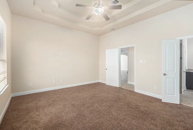an empty room with a chandelier fan and windows