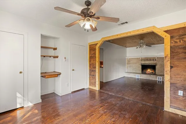 an empty room with wooden floor a ceiling fan and a kitchen