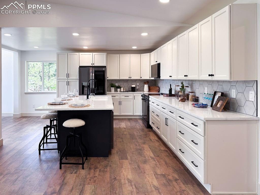 14546 Pine View Road Larkspur, CO 80118 - Photo 4 of 37 Kitchen with black appliances, a kitchen bar, backsplash, dark wood-style flooring, and recessed lighting